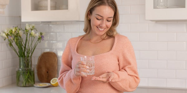 Frau mit Kapseln & einem Glas Wasser
