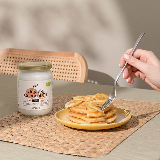 Hand hält Gabel und nimmt Pancakes daneben Kokosöl von nu3