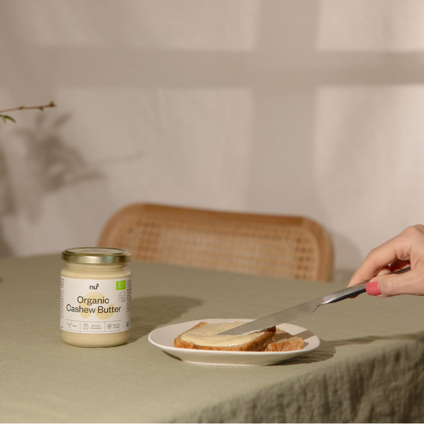 Cashewmus steht auf dem Tisch neben einem Brot, das mit Nussmus geschmiert wird