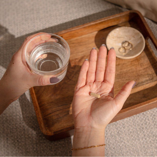 kapseln in der Hand mit einem Glas Wasser