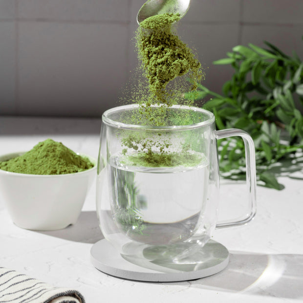 Glas mit Wasser und grünen Pulver in einer Schale