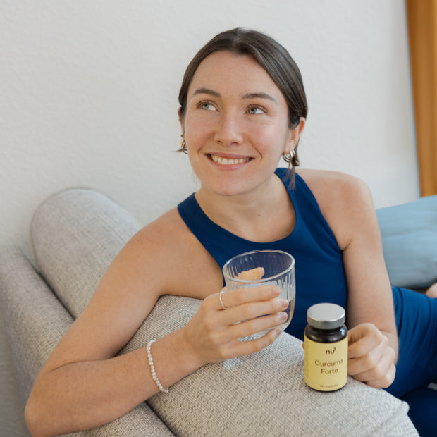 Frau sitzend auf dem Sofa mit einem Glas Wasser und Kapseldose